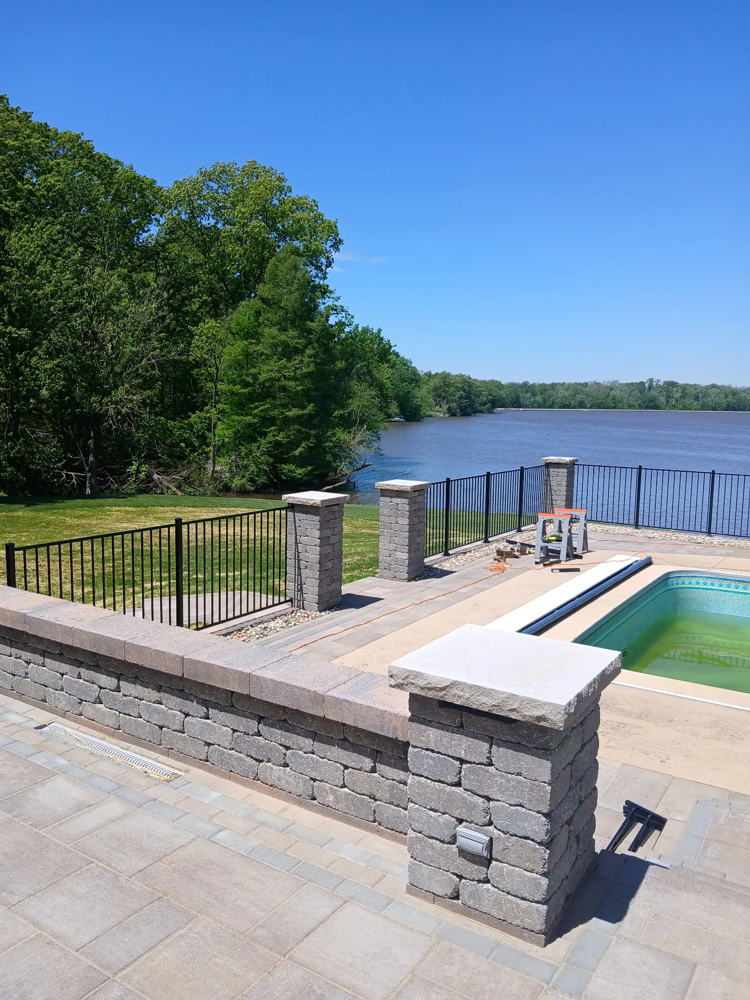 Black metal pool fencing with stone columns overlooking a lake.